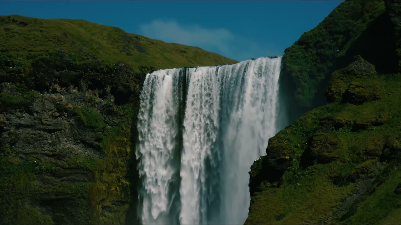 A tall waterfall pouring between green, mossy cliffs under a blue sky